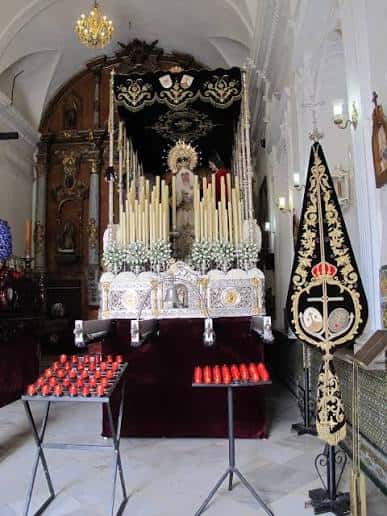 Interior de la capilla mostrando el altar principal con velas, ornamentos religiosos y detalles barrocos en la decoración