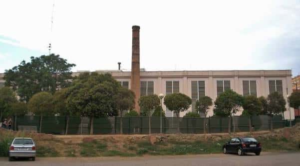 Vista lateral del complejo cultural con chimenea industrial y entorno arbolado