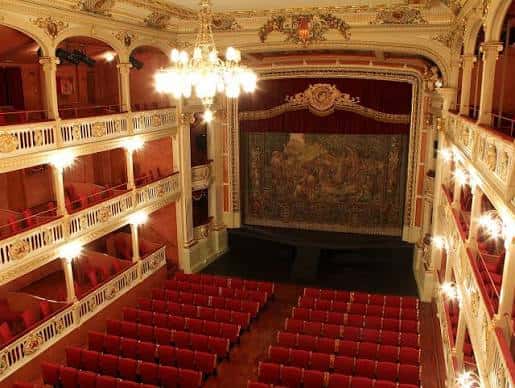Escenario con telón decorativo y butacas rojas desde la perspectiva de la platea