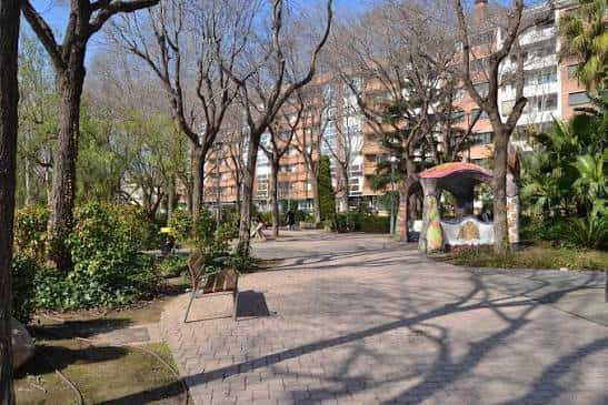 Paseo arbolado en el Parc de Sant Jordi con bancos y edificios residenciales al fondo