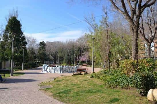 Área central del parque con escultura blanca y senderos peatonales bajo cielo despejado