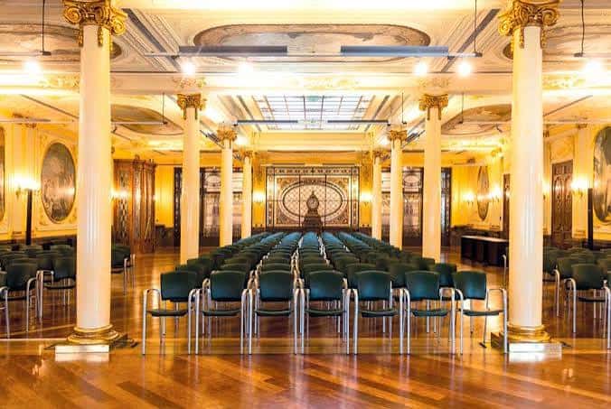 Gran salón de actos con columnas doradas y suelo de madera
