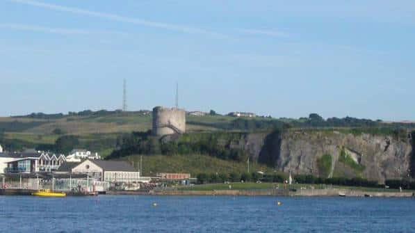 Torre Mount Batten desde la bahía, con edificios costeros y acantilados en primer plano