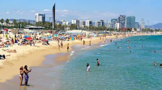 Playa del Bogatell con personas en el agua y la ciudad al fondo