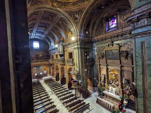 Interior de la basílica con nave central, bancos de madera y retablo ornamental