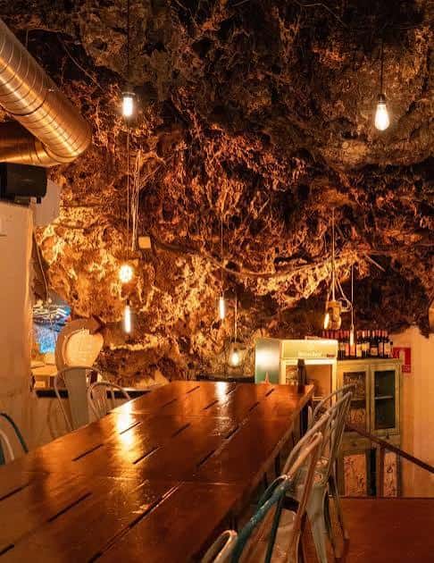 Interior de la cueva con iluminación cálida y mesas de madera