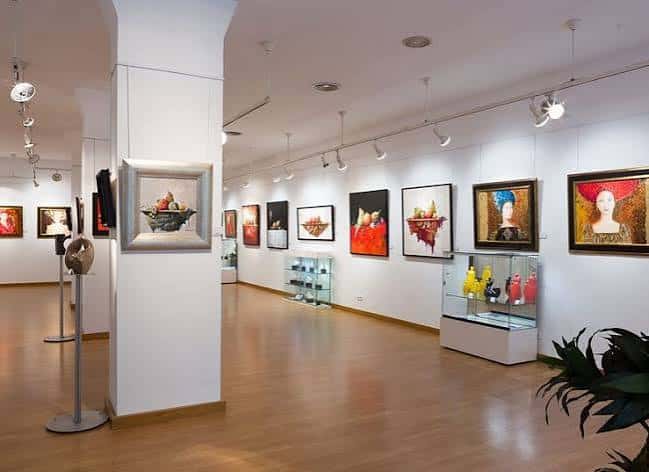 Interior de la galería con obras de arte expuestas en paredes blancas y vitrinas de exhibición
