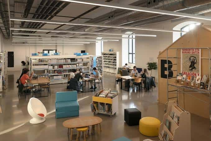 Espacio interior de Medialab con personas trabajando, mobiliario moderno y estanterías de libros