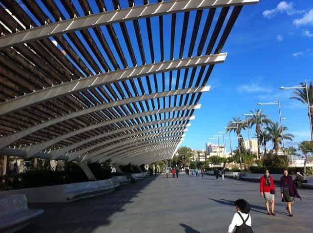 Detalle arquitectónico de la cubierta ondulada del paseo con personas caminando bajo ella