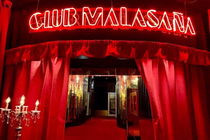 Entrada del Club Malasaña con cortinas rojas y letrero de neón