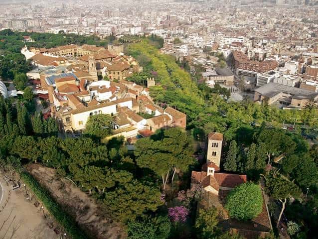 Vista aérea del Poble Espanyol rodeado de vegetación y la ciudad de Barcelona al fondo