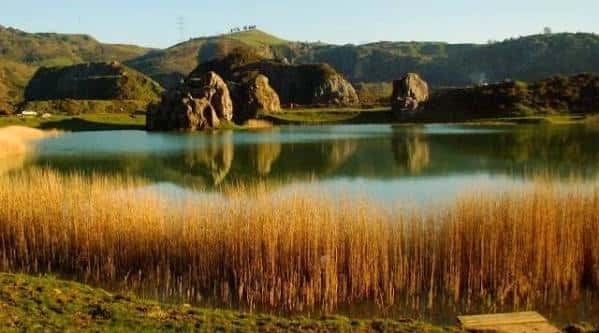 Lago tranquilo con juncos dorados y formaciones rocosas en Montes de Triano