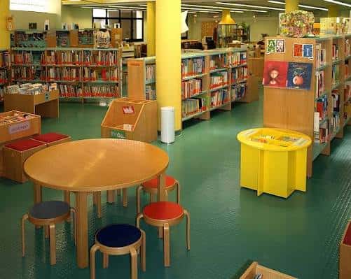 Sala infantil de la biblioteca con estanterías coloridas y mesas redondas