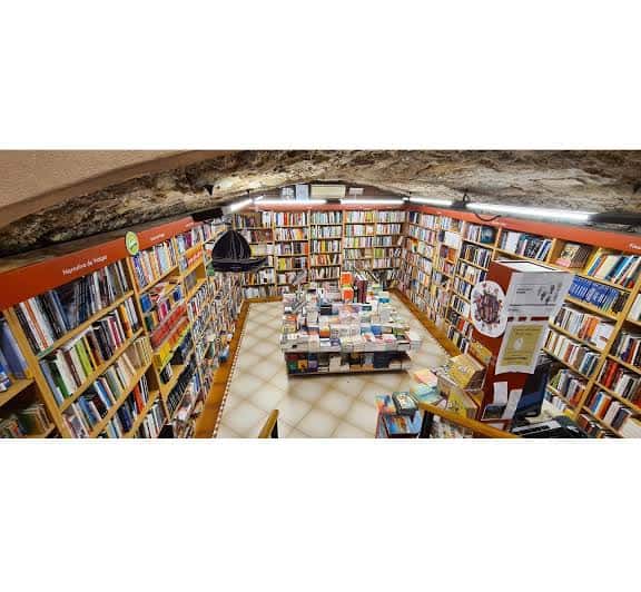 Vista panorámica del interior de la librería Caselles con estanterías llenas de libros y techo de piedra