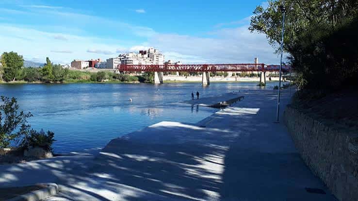Paseo fluvial junto al río Ebre con el puente rojo de fondo