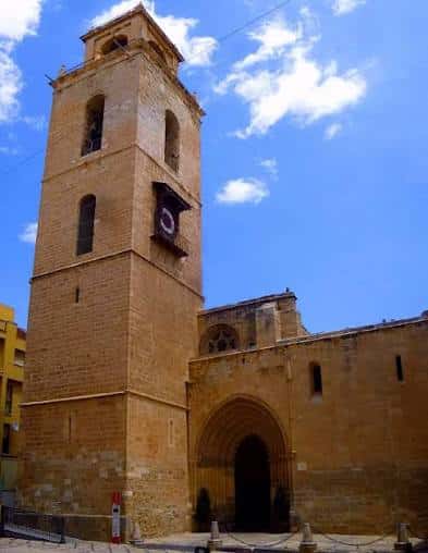 Vista exterior de la Catedral del Salvador y Santa María en Orihuela, destacando su torre campanario de ladrillo bajo un cielo azul