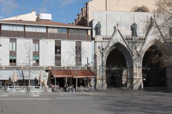 Detalle de la entrada gótica y plaza con mesas de cafetería en primer plano