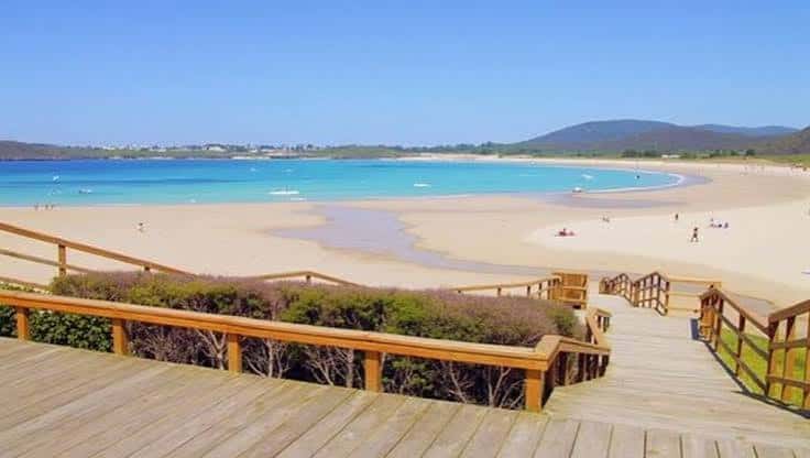 Vista panorámica de la playa San Xurxo con pasarela de madera y mar turquesa
