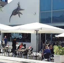 Fachada del Estruch Bar con escultura de pez y mesas al aire libre