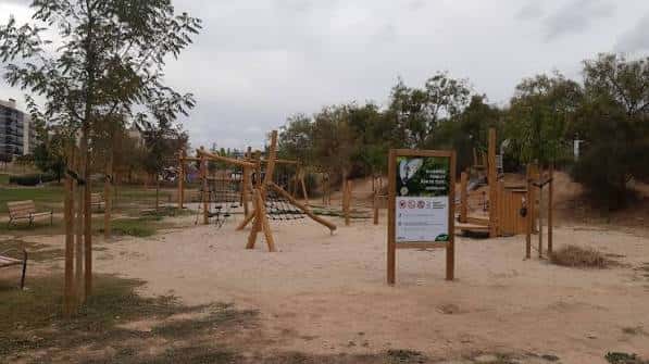 Área de juegos infantil en el parque Joan Oró con estructuras de madera y zona de arena