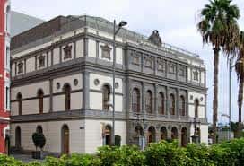 Fachada exterior del Teatro Pérez Galdós con palmeras y cielo nublado