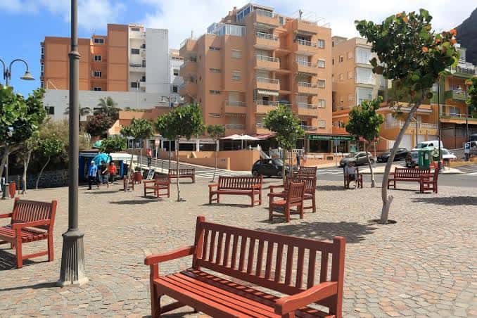 Plaza de Bajamar con bancos de madera, árboles y edificios residenciales al fondo