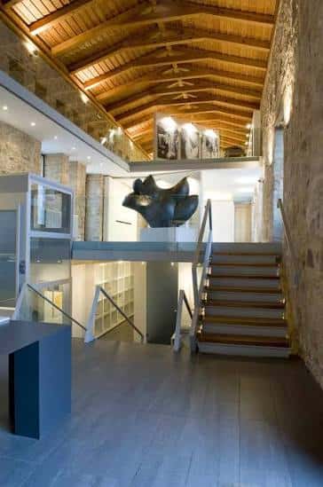 Interior del museo con escalera de madera, vigas de techo y escultura central en el atrio