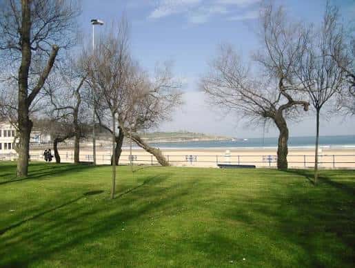 Área verde del parque con vista al mar y playa de fondo
