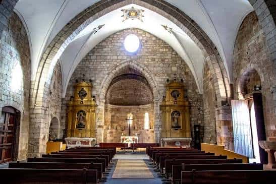 Interior de la iglesia con bóvedas de piedra y retablos dorados