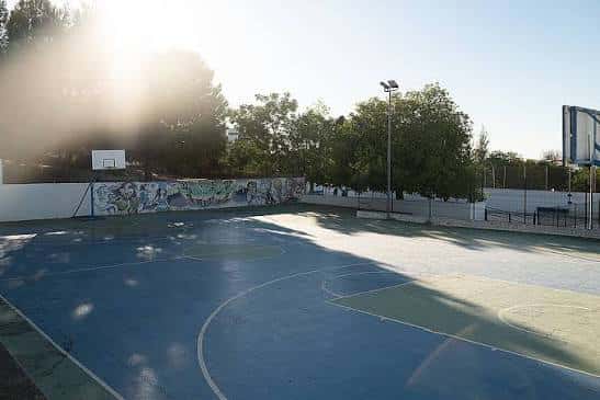 Pista de baloncesto al aire libre con murales artísticos y sol de fondo