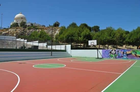 Pista deportiva exterior con césped sintético y vista del faro de Chiclana al fondo