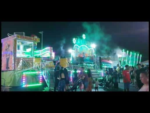 Vista nocturna del recinto ferial con atracciones iluminadas y público