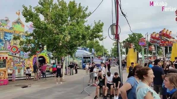 Ambiente festivo en el recinto ferial con atracciones y público caminando