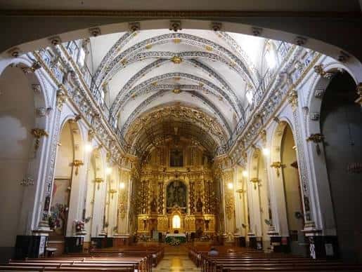 Interior de la iglesia con bóvedas decoradas y retablo dorado