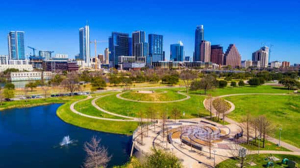 Vista del parque con el lago, senderos curvos y el skyline de Austin al fondo
