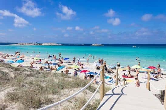 Playa concurrida de Playa d'en Bossa con sombrillas y bañistas bajo un cielo despejado