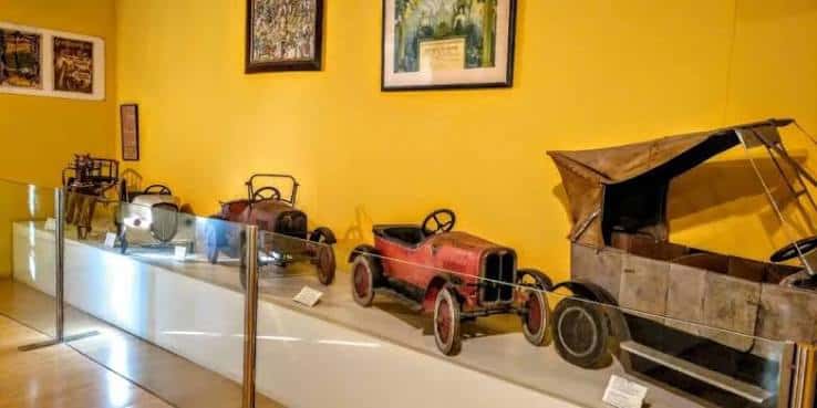Exposición de juguetes históricos en exhibición dentro del museo, incluyendo coches de pedal antiguos