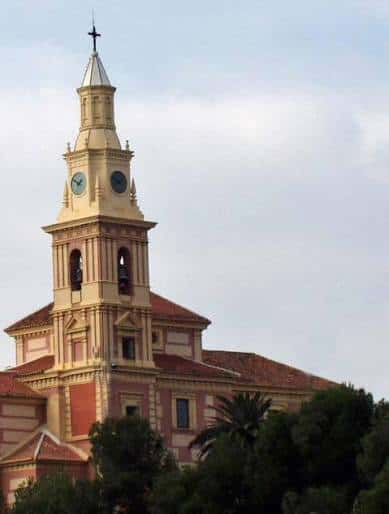 Detalle de la torre del Templo de Poniente en Motril, mostrando el reloj y la cruz en la cúspide