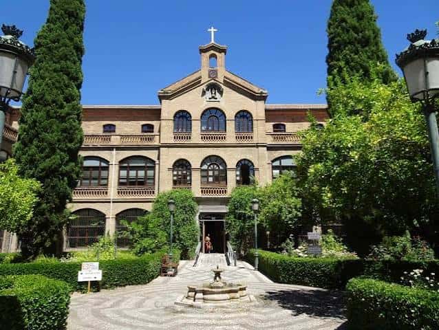 Fachada principal del edificio rodeado de vegetación y farolas clásicas