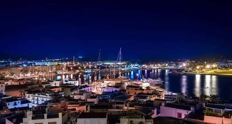 Vista nocturna del puerto de Ibiza con reflejos en el agua y ciudad iluminada