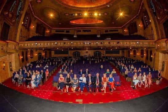 Grupo de personas posando en el escenario del teatro durante un evento
