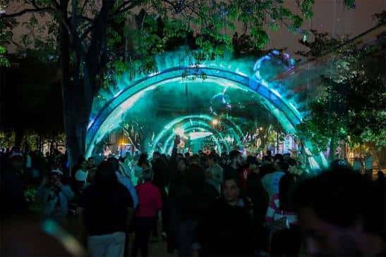 Túnel de luces en el Parque de la Paz con personas caminando bajo arcos iluminados