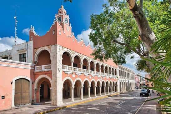 Vista exterior del Palacio Municipal de Mérida con su característica fachada rosa y arcos coloniales bajo un cielo azul