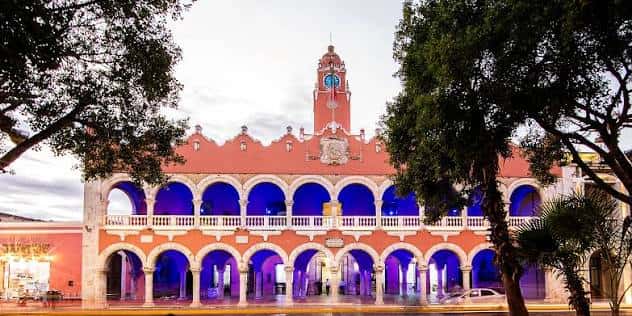 Fachada del Palacio Municipal de Mérida iluminada con luces azules durante la noche, creando un ambiente festivo