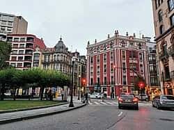 Plaza de San Miguel en Gijón con tráfico urbano, semáforos y fachadas coloridas de edificios emblemáticos