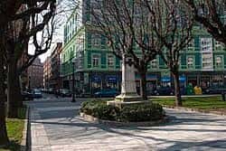 Monumento central en la Plaza de San Miguel rodeado de árboles sin hojas y edificios verdes de estilo moderno