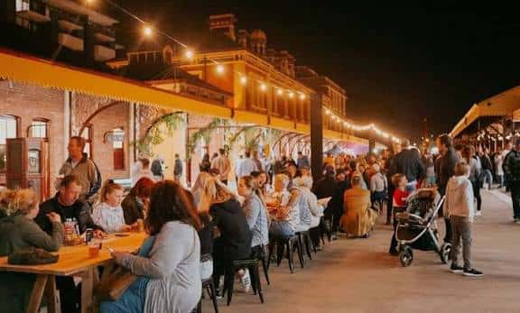 Ambiente nocturno en The Station con mesas al aire libre y luces decorativas