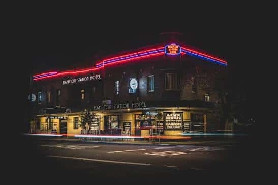 Fachada del Hamilton Station Hotel iluminada con luces de neón durante la noche