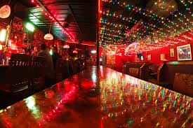 Interior del bar con barra de madera y luces de colores