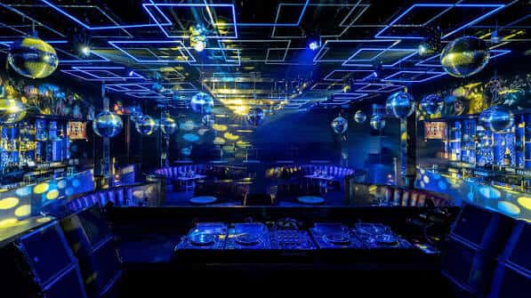 Vista del área de DJ y barra con luces azules y esferas reflectantes
